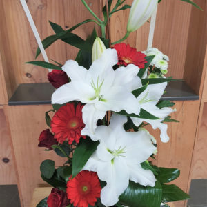 Composition en hauteur dans les tons rouge et blanc, composé de lys, de roses, de gerberas et de santinis